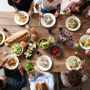 overhead photo of a group of people gathered together to eat dinner. There are lots of plates of food and drinks around the table.