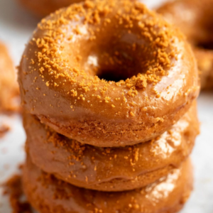 a stack of 3 glazed donuts with biscoff crumbs on them