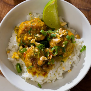 A bowl of rice and meatballs in a creamy sauce with a slice of lime.