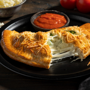 a cheese calzone open on a black plate with a side of sauce