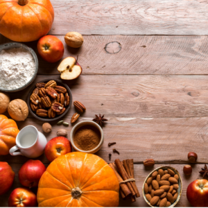fall pumpkins, apples, nuts, cinnamon sticks, spices and a bowl of flower on a wood plank table