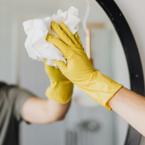 someone cleaning a mirror with a paper towel and wearing a yellow rubber glove