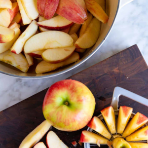 Sliced apples in a metal bowl, with whole apple and sliced segments arranged on a dark wooden board nearby.
