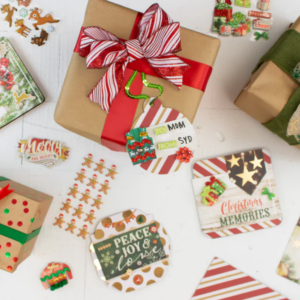 Top-down view of a tabletop with a red-and-white holiday gift wrap, small wrapped packages, and scattered festive cards and decorations arranged around a central gift.