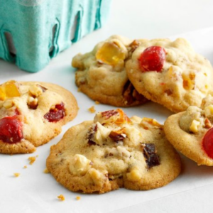 Assorted freshly baked cookies on a white plate, including fruit-filled and nutty dough pieces, with crumbs and a few scattered bits of fruit on the surface.
