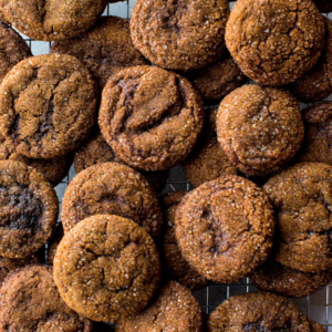 Close-up of a pile of round, sugar-dusted, brown coloured cookies with a crinkled texture, filling the frame.