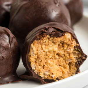 Close-up of a sliced chocolate dessert ball showing a golden, crumbly filling with dark chocolate exterior, with more rolls in the background on a white plate.