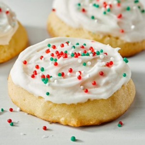 Two cookies on a light surface, topped with white icing and colorful red-and-green sprinkles, with some sprinkles scattered in the foreground.