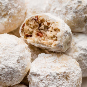 Powdered sugar–coated pastries with a cross-section showing a crumbly nut and filling center, stacked on a light, flour-dusted surface.