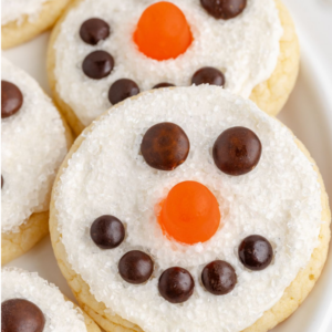 A close-up of cookies topped with frosting, chocolate candies and an orange jube jube arranged on top to look like a snow man's face.