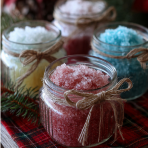 Decorative glass jars and a small bowl filled with colourful sugar body scrub, with a patterned red-and-gold plaid background.